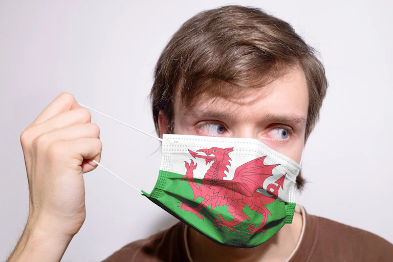 A man putting on a covid facemask bearing a Welsh flag design.