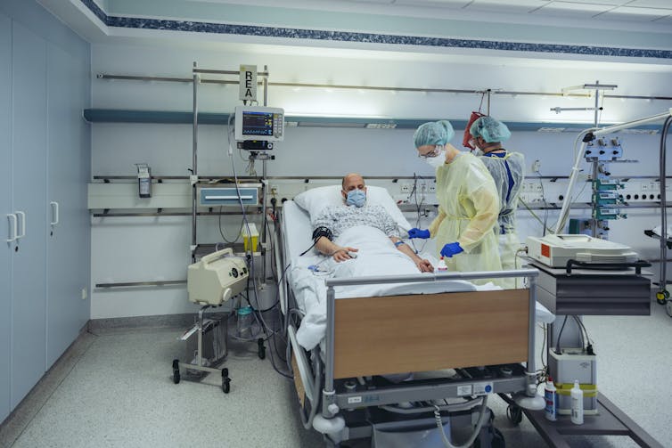 A doctor treating a patient in a hospital bed, both wearing masks.