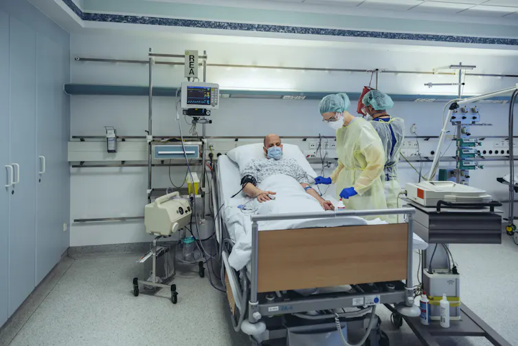 A doctor treating a patient in a hospital bed, both wearing masks.