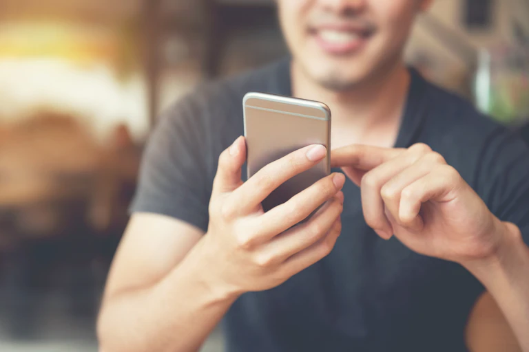 A young man smiles looking at his smartphone.