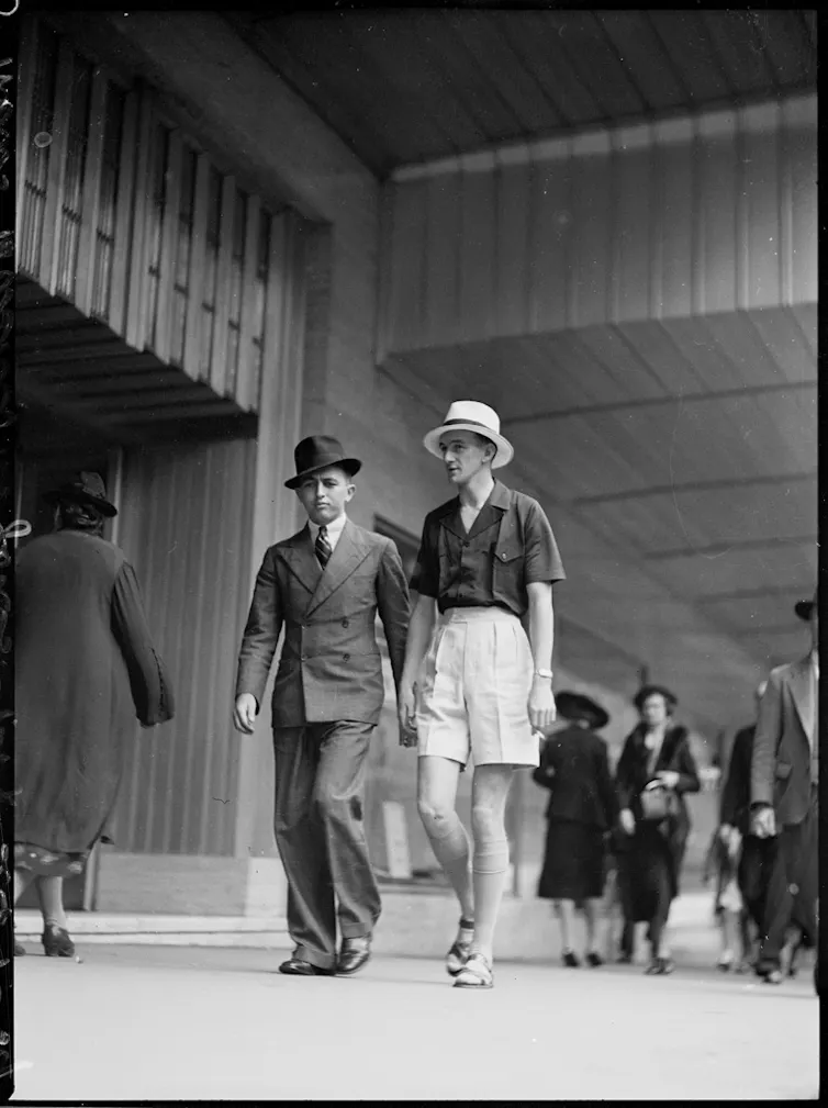 Two men walk down street in fashion suits of 1930s.