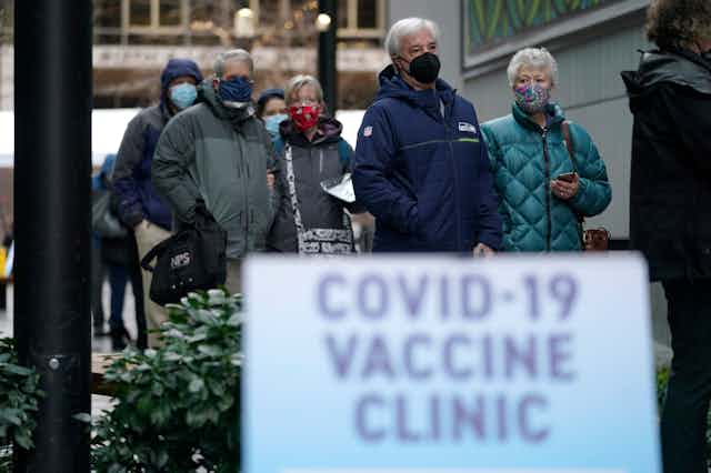 People wearing masks waiting in line to receive a COVID-19 vaccine
