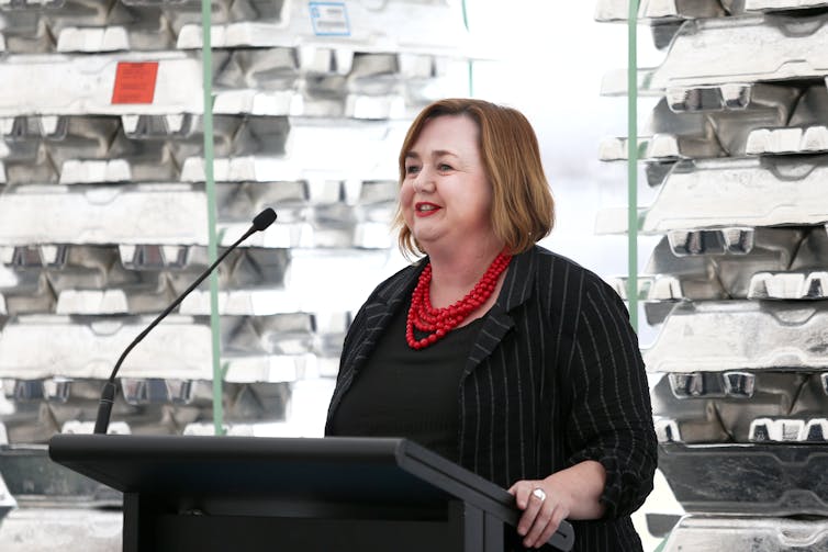 Megan Woods speaking in front of aluminium ingots.