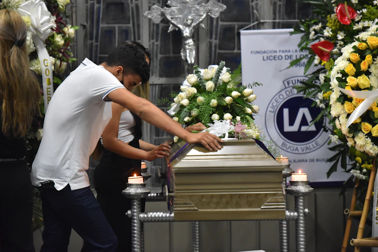 Man in white t-shirt leans on a coffin with flower displays at a church in Buga, Valle del Cauca, Colombia.