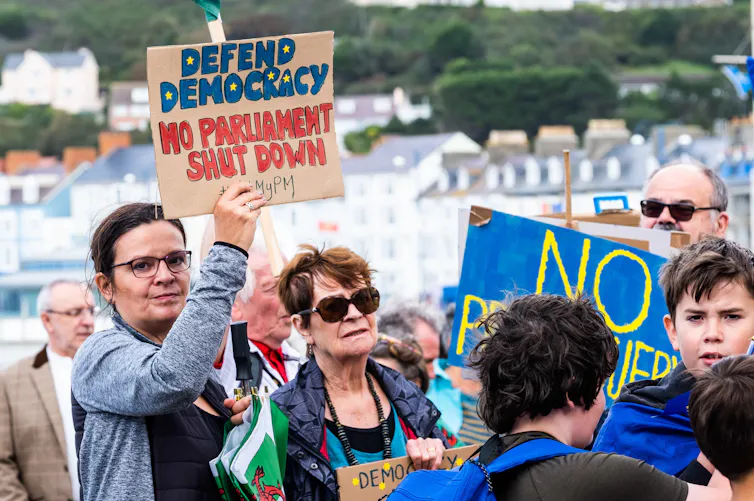 A woman at a 2019 protest again parliamentary prorogation holds a sign reading 'defend democracy, no parliament shut down'.