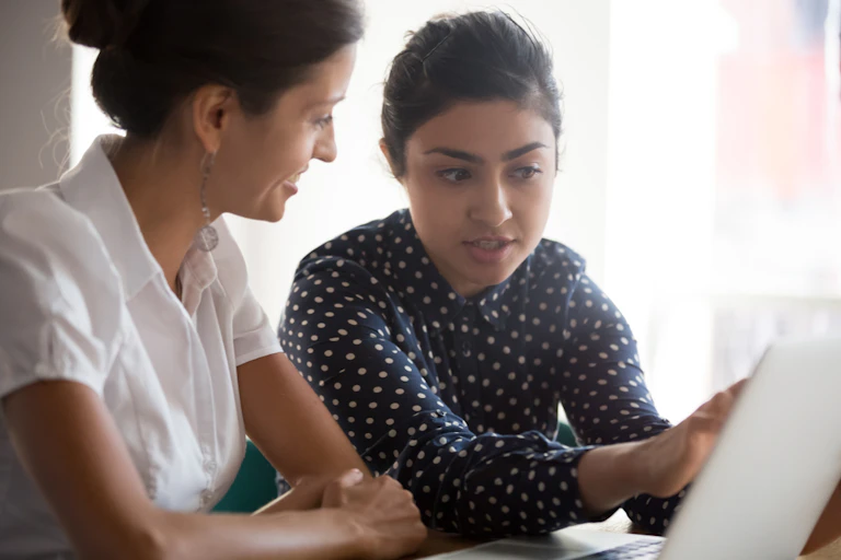 Female businesswoman listens as mentee young woman shows project online