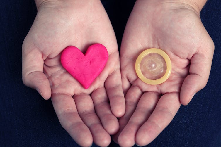 Open palms holding a heart shape and a condom.