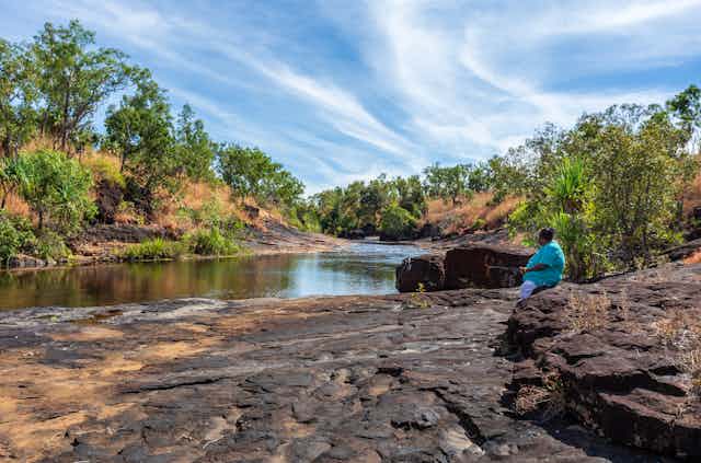 Indigenous woman sits and looks at river