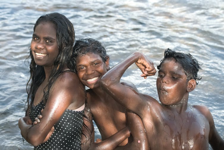 Three Indigenous children smiling in water