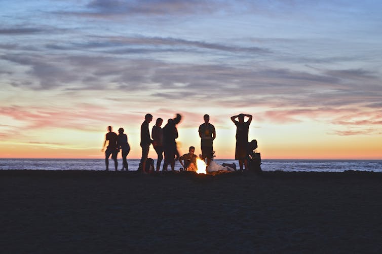 Silhouettes of young people on a beach, in the evening around a fire.
