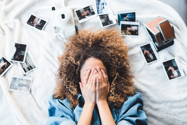 Young woman lying on bed with photographs around her.