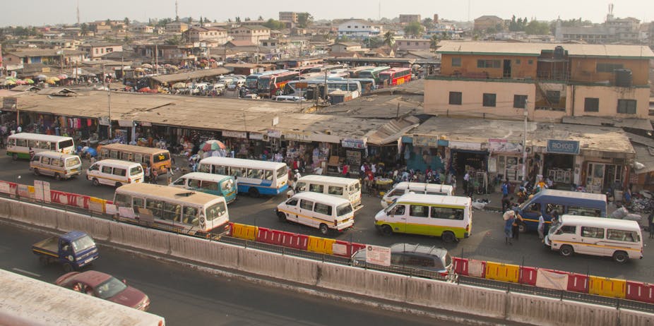Vehicles, most of them minibuses, line up alongside a series of small structures from which people can board the vehicles