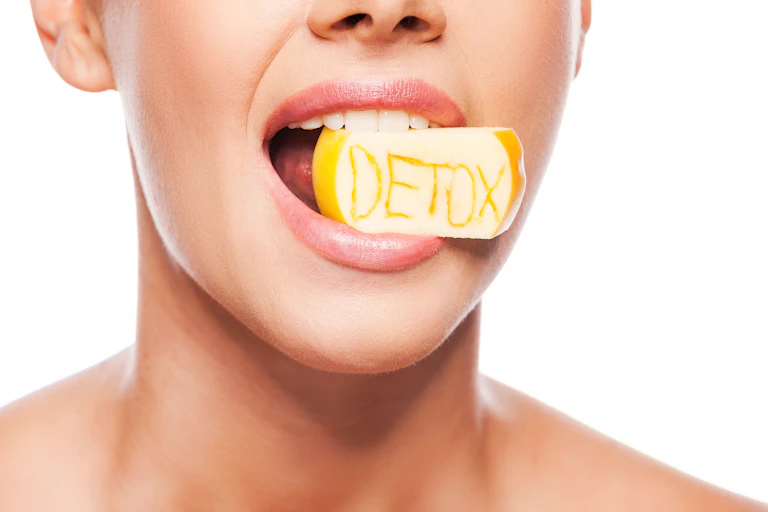 Rostro de una mujer con un trozo de manzana con la inscripción detox en la boca