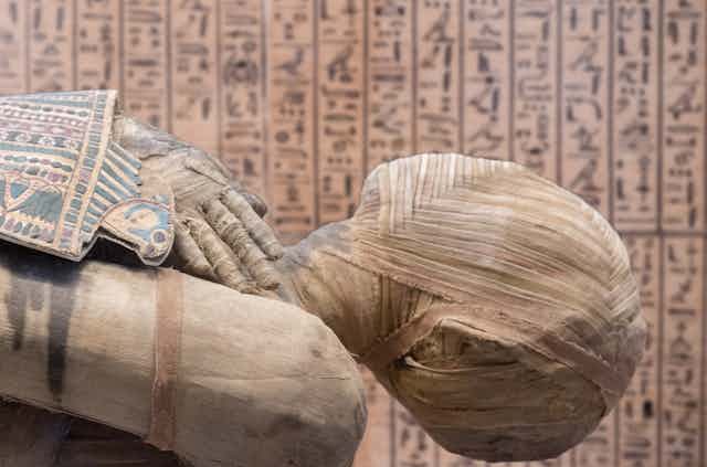Close up of an Egyptian mummy with hieroglyphics in the background.