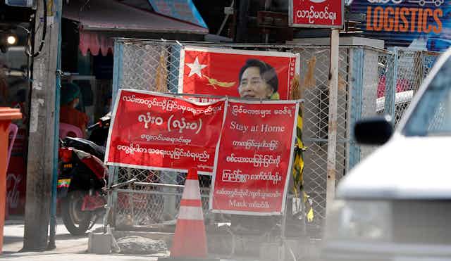 Signs in Burmese and ENglish telling people to stay at home obscure an NLD election poster.