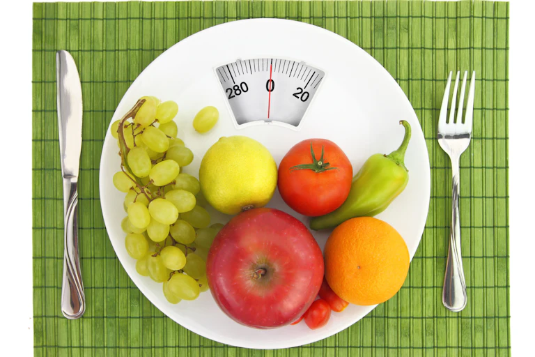 Healthy fruits and vegetables on a scale with a knife and fork on either side.