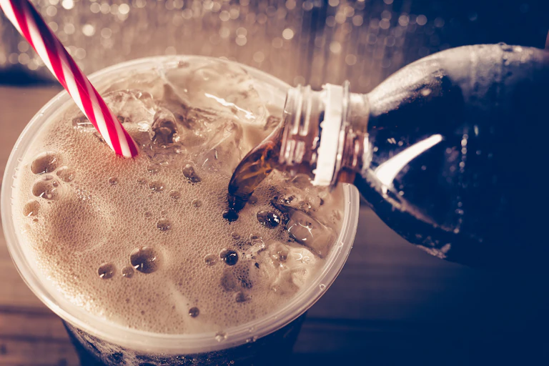 Fizzy drink being poured from a bottle into a cup, with a straw sticking out