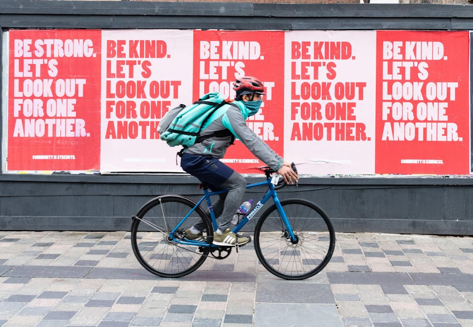 A man rides a bicycle past posters.