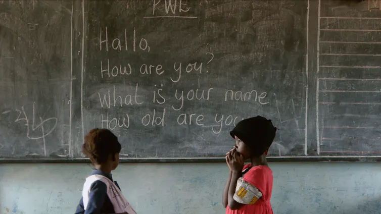 Two children in front of a blackboard showing English phrases.