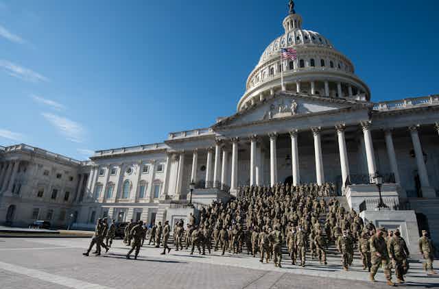 Zoomed out image of Capitol with dozens or hundreds of soldiers in camoflauge descending steps