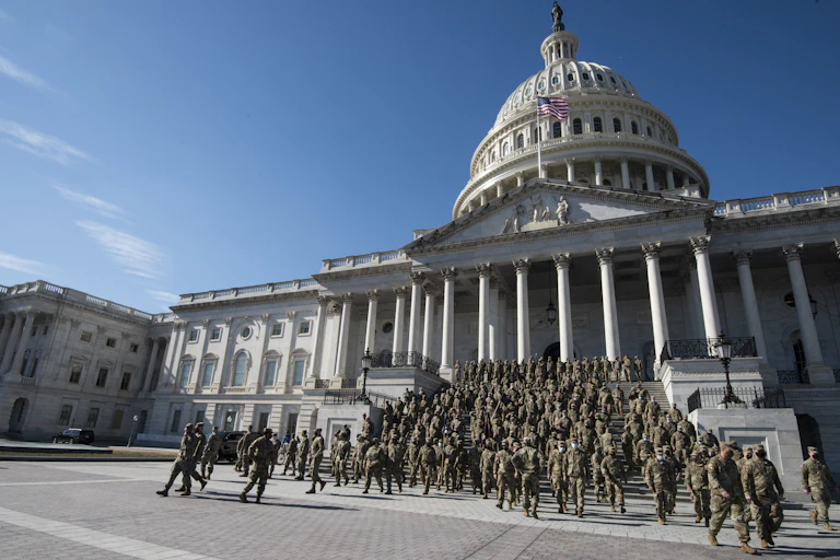 Zoomed out image of Capitol with dozens or hundreds of soldiers in camoflauge descending steps