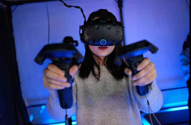 A woman plays a video game with a VR headset and consoles in both hands.