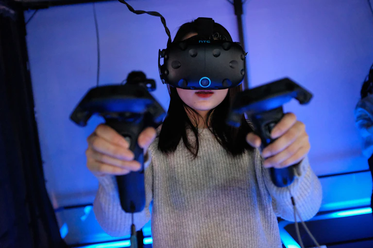 A woman plays a video game with a VR headset and consoles in both hands.