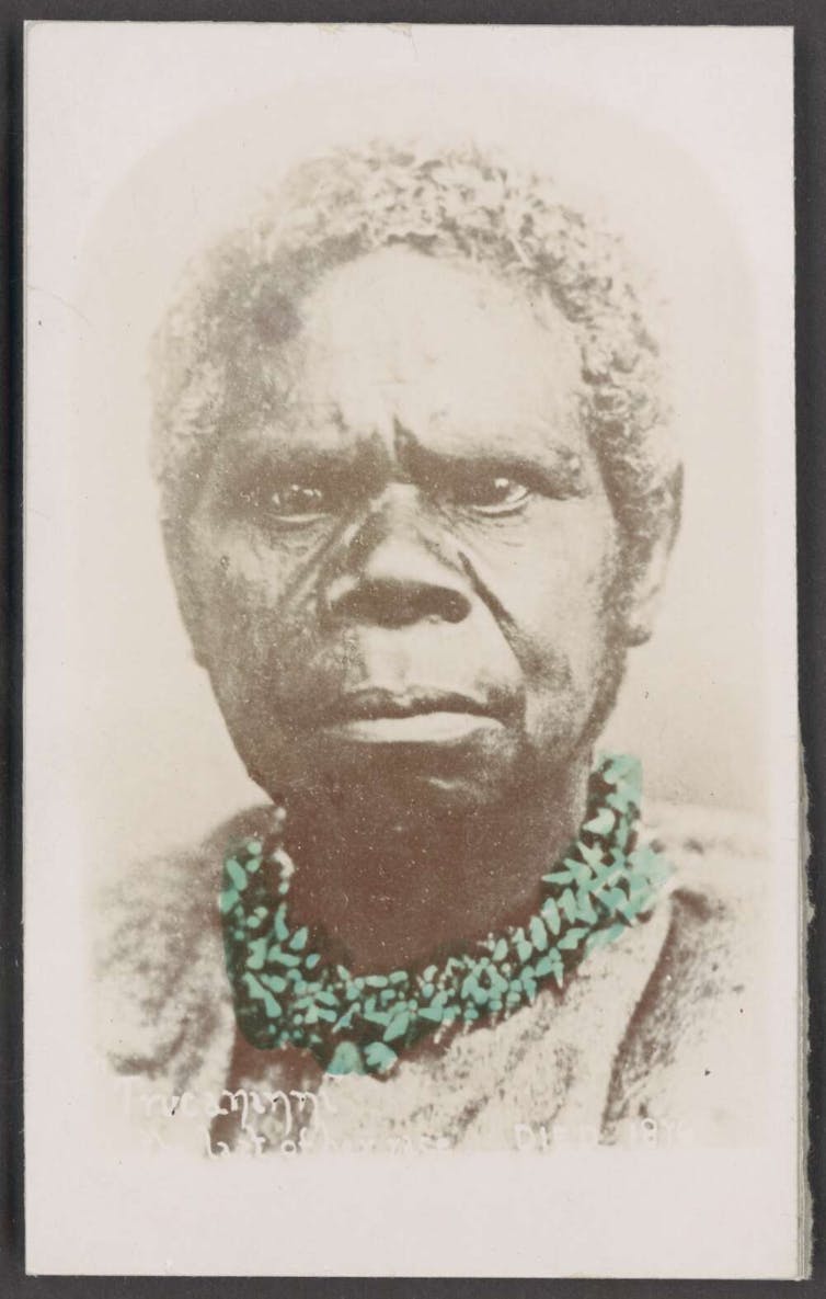 Woman stares straight to camera. She wears a necklace of shells.