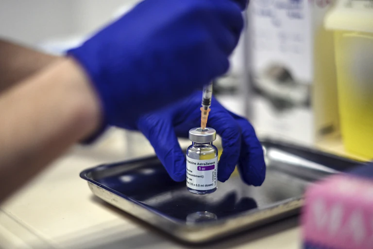 Gloved hands fill a syringe from a vial of the AstraZeneca vaccine.