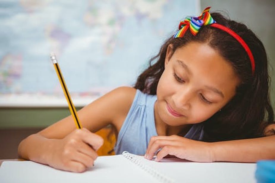 Seorang anak perempuan menulis di buku dengan pensil
