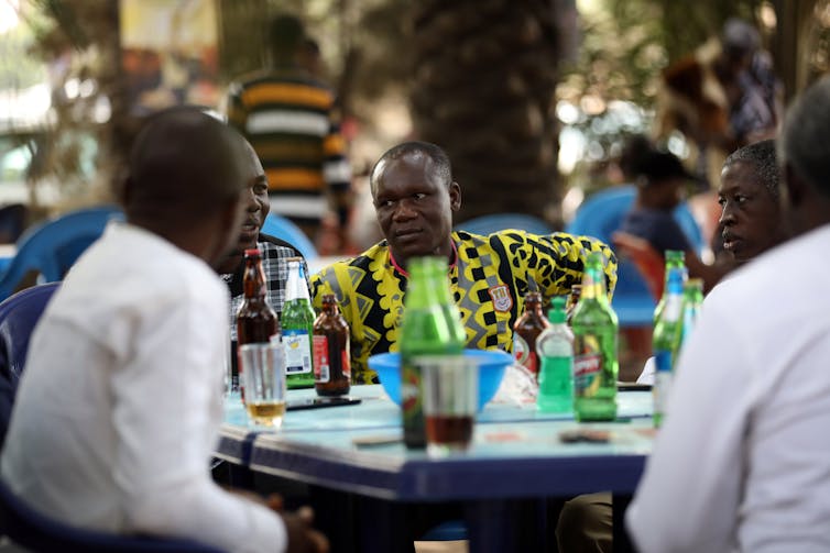 A group of men at a table packed with bottles.