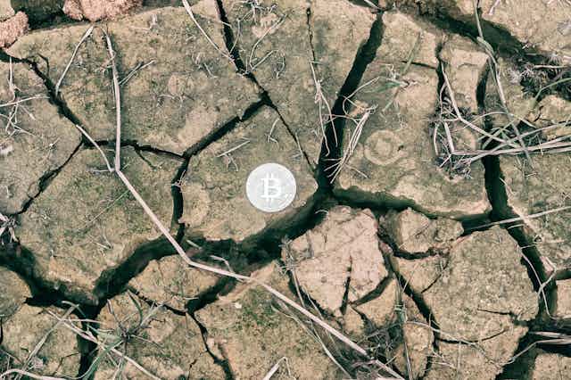 A silver bitcoin on parched, cracked soil.