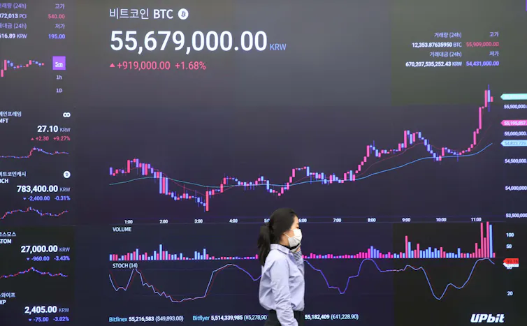 A woman walks past an electronic screen broadcasting the price of bitcoin.