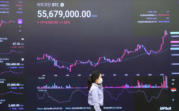 A woman walks past an electronic screen broadcasting the price of bitcoin.