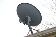 A satellite dish on a roof with bare tree limbs in the background