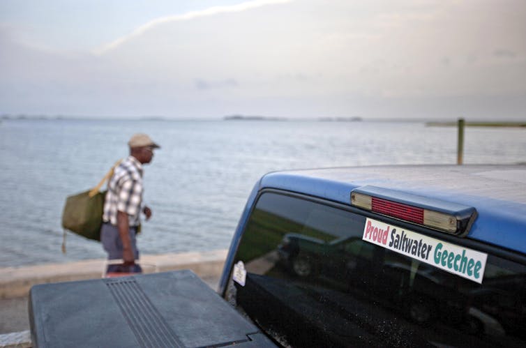 A sticker celebrating the Geechee heritage is seen on a pickup truck as passengers board a ferry.