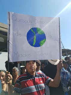 A man holds a sign in Spanish with a drawing of Earth.