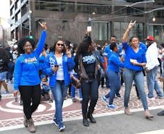 Several African American women dressed in blue walk together.
