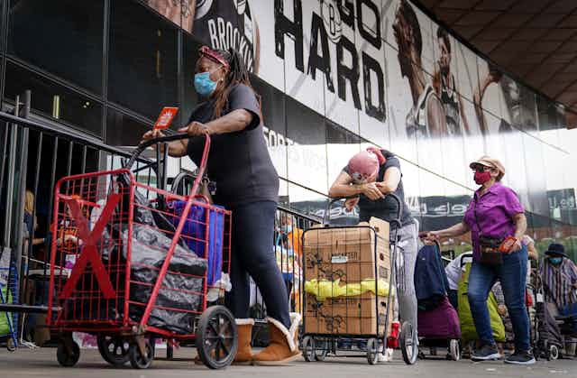 Pedestrians wait in line with carts to collect fresh produce and shelf-stable pantry items outside Barclays Center in New York City