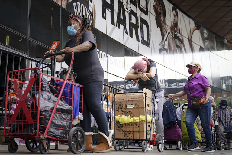 Pedestrians wait in line with carts to collect fresh produce and shelf-stable pantry items outside Barclays Center in New York City