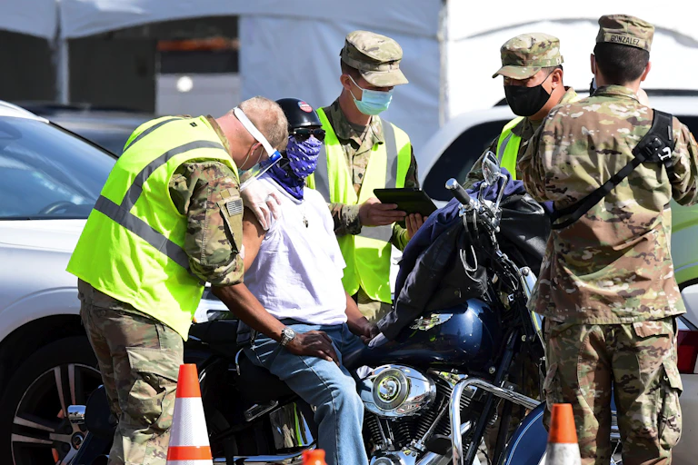 A man on motorcycle gets a vaccine shot from National Guard troops.