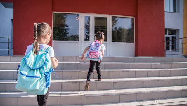 Two young girls walking up the school steps.