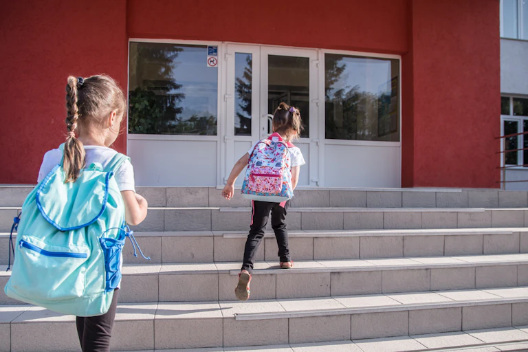 Two young girls walking up the school steps.