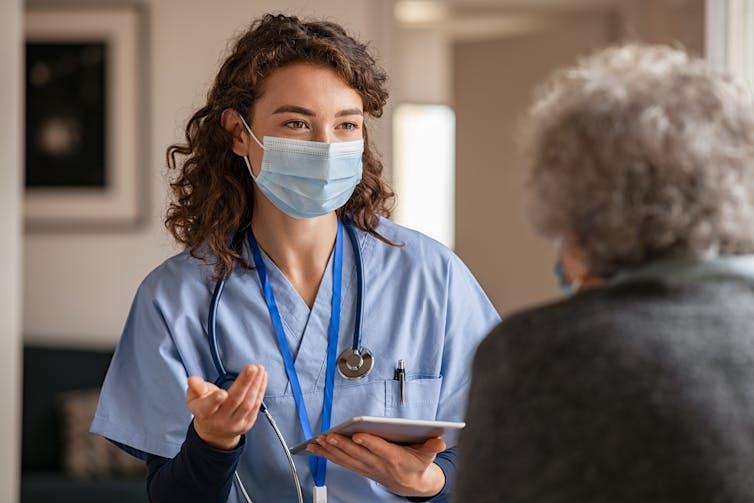 A health-care worker wearing a mask talks to an elderly person.