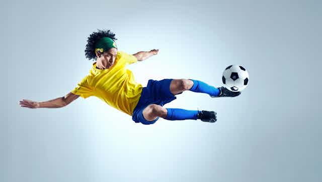 Un futbolista en el aire con la equipación de Brasil chuta un balón.