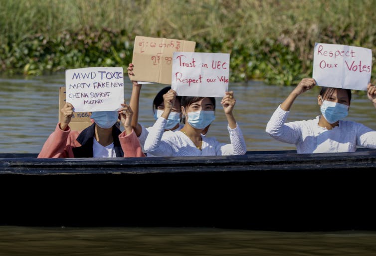 Women in masks carry placards as they sit in a boat.