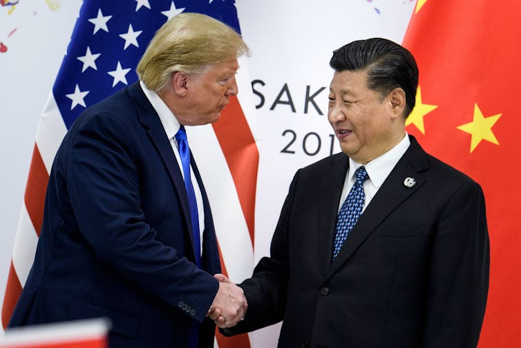 Trump and Xi shake hands in front of a Chinse and American flag
