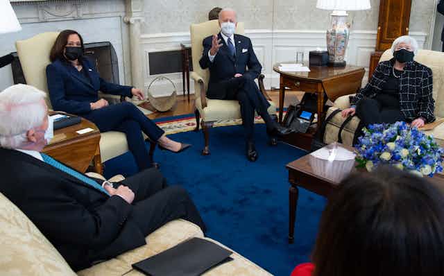 Biden sits with Harris and Yellen in the Oval Office, all wearing masks.