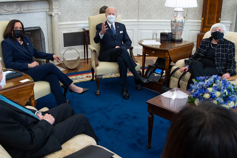 Biden sits with Harris and Yellen in the Oval Office, all wearing masks.