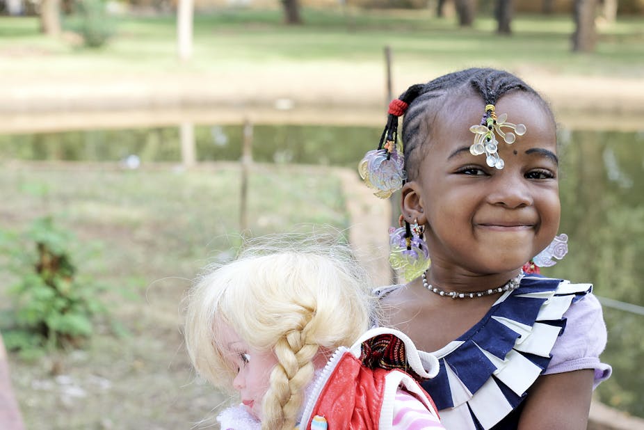 A little Black girl smiles as she is holding a white doll. 
